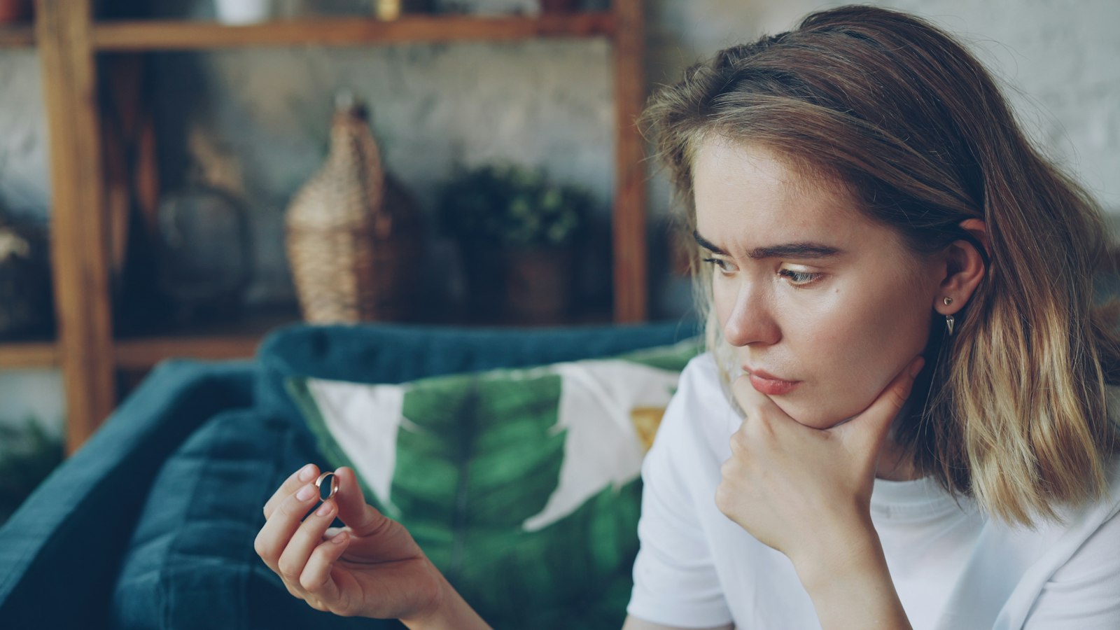 A woman sitting alone at home, looking at a ring in her hand